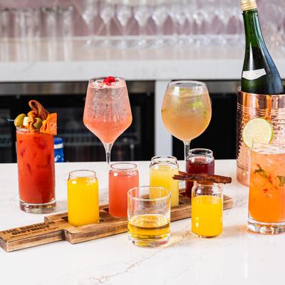 A variety of cocktails and a bottle of sparkling wine on a bar counter.