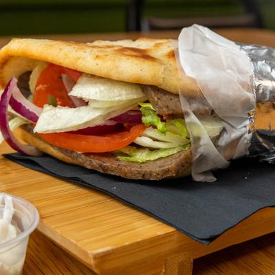 Gyro sandwich wrapped in pita bread and served with a side of tzatziki sauce.