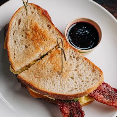 Toasted breakfast sandwich with bacon served alongside berry jam.