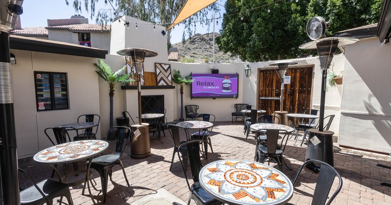 Outdoor patio with mosaic-tiled tables and black chairs set atop brick flooring