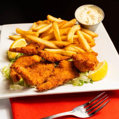 Fried fish served over lettuce with fries, tartar sauce, and lemon wedges