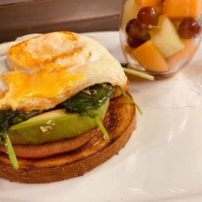 Open-faced sandwich topped with fried egg, avocado and spinach, served with fresh fruit.