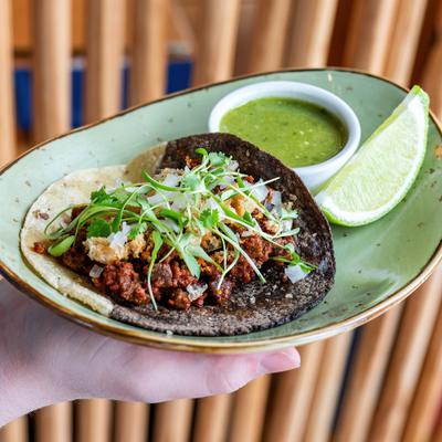 Chorizo taco on a two-tone corn tortilla with herbs, lime, and green salsa.