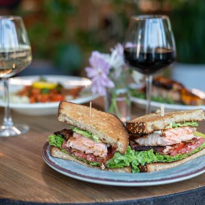 Salmon BLT sandwich served with two glasses of wine.