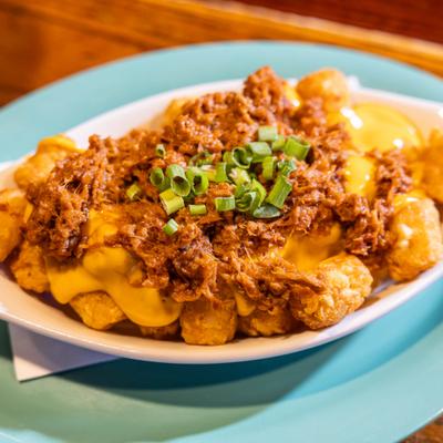 Loaded tater tots topped with cheese sauce, shredded meat and green onions.
