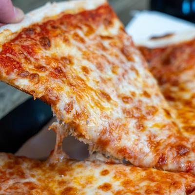 A slice of classic cheese pizza being lifted from a whole pizza.