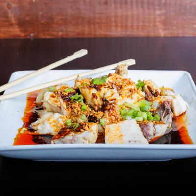 Spicy chicken topped with chili oil, crushed peanuts, and scallions on a white plate.