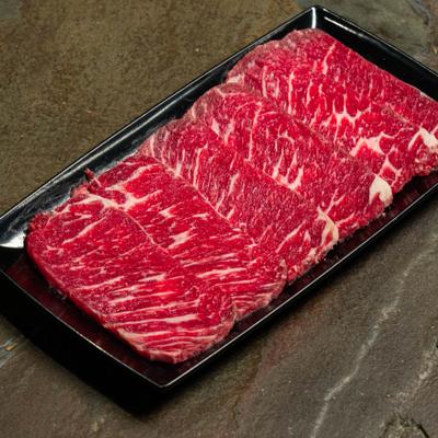 Raw short rib slices arranged on a black plate.