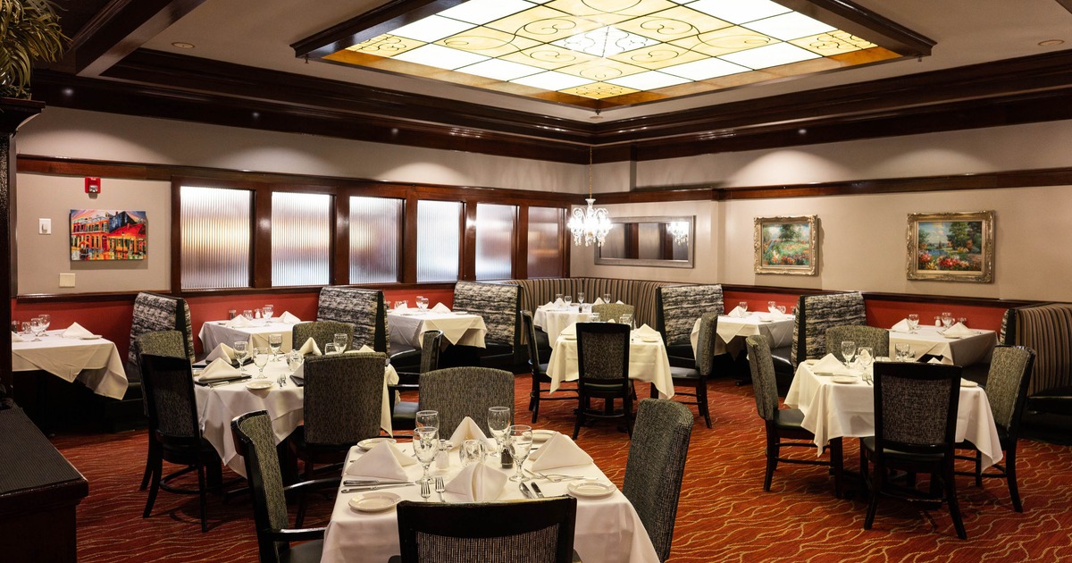 Elegant restaurant interior with tables, booths, a chandelier, and a stained-glass ceiling