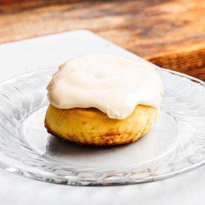 Frosted cinnamon roll on a clear glass plate.