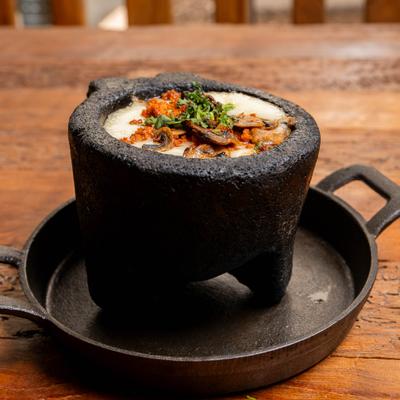 Queso Fundido topped with  mushrooms and chorizo, served in a volcanic rock bowl.