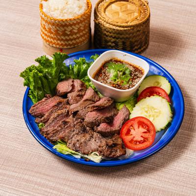 Sliced grilled beef with vegetables, dipping sauce,  and a side of rice.