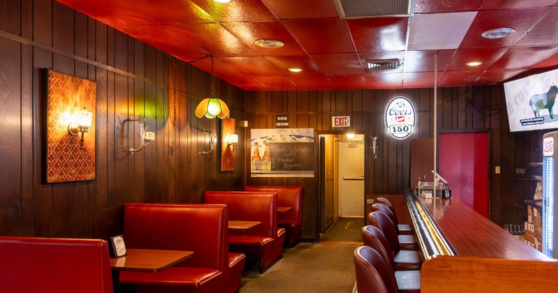 A room featuring wooden walls, red ceiling, red booths and bar top with bar chairs