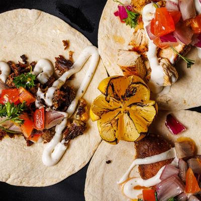 Three tacos with assorted toppings drizzled with sauce and garnished with a grilled lemon.
