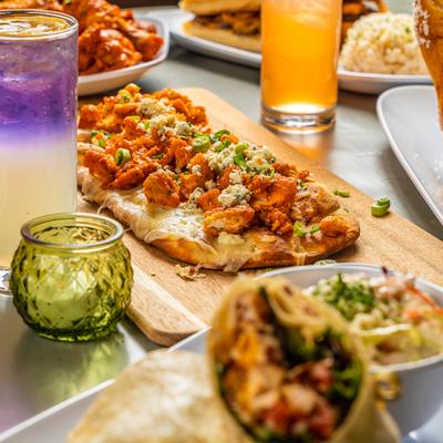 Buffalo chicken flatbread surrounded by drinks and other dishes.