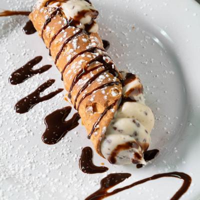 A cannoli drizzled with chocolate sauce.