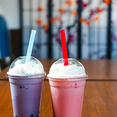 Two bubble tea drinks, one purple and one pink, sit on a wooden table.