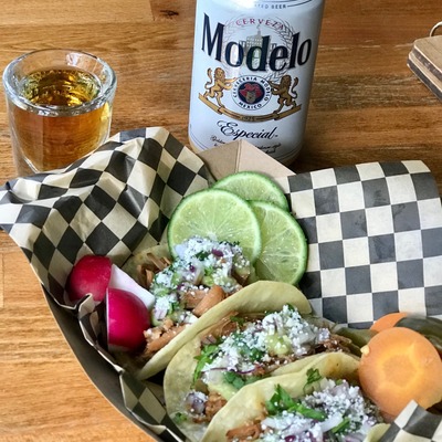 Tacos served with a can of Mexican beer and a shot of gold tequila.