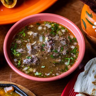 Mexican soup in a pink bowl with drinks and a quesadilla on a wooden table