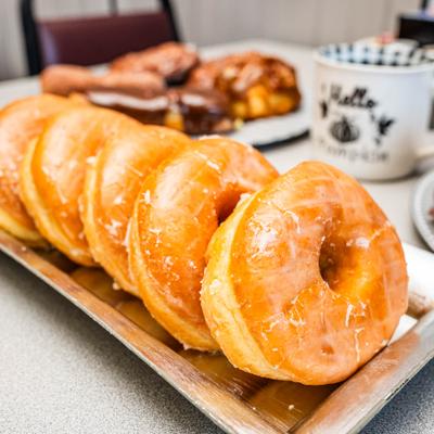 Plate of glazed donuts served alongside other pastries and a cup of coffee.