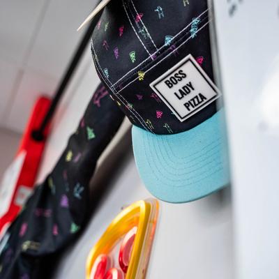 Branded cap with a colorful pattern and a blue section hanging on a wall.