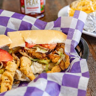 Soft Shell Crab Po-boy served on the table with a drink and loaded potato.