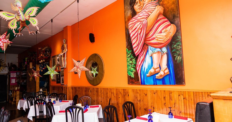 Tables set for dining by an orange wall with a large painting and decorations