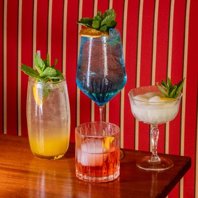 Elegant cocktails with citrus and mint garnishes on a table against a red striped wall.