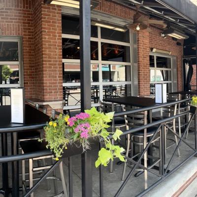 Fenced outdoor patio seating area with tables and chairs against a brick wall.