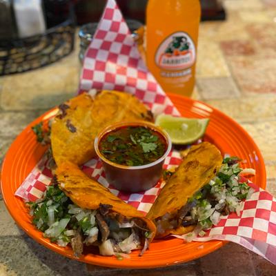 Tacos Birria on a table with a Mexican soda.