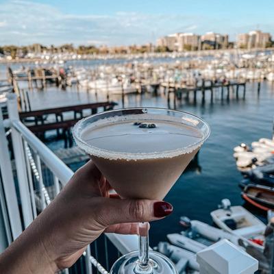 Hand holding a Espresso Martini cocktail with marina view in the background.