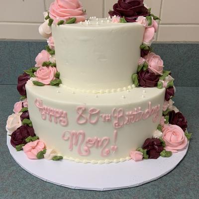 A two tiered birthday cake adorned with delicate pink and maroon flowers tiered cakes