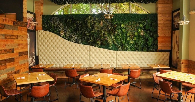 Interior, tables and chairs, button tufted seating and tables beside a wall decorated with greenery
