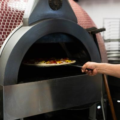 A hand using a pizza peel to place a pizza in the oven.