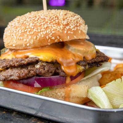 Cheeseburger with two patties, red onion, lettuce and tomato on a sesame seed bun.