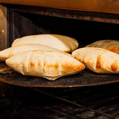 Four puffed, golden-brown pita breads rest on a wire cooling rack inside an oven.