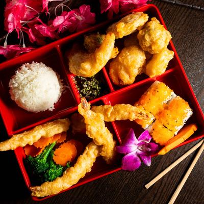 Japanese bento box with shrimp tempura, sushi rolls, steamed rice, and vegetables.