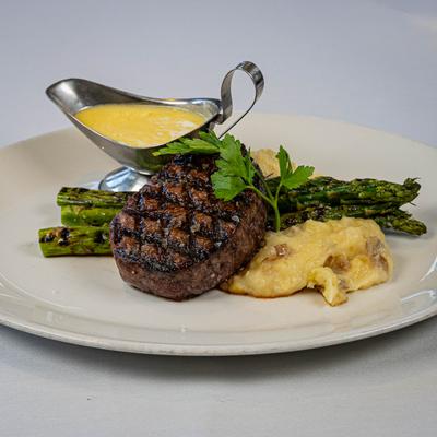 Grilled steak with asparagus and mashed potatoes; a gravy boat of yellow sauce.