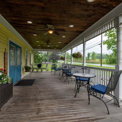 Exterior, wooden porch with tables and chairs, blue cushions, and ceiling fans.