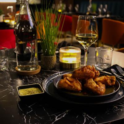 Chicken wings with a side of dip, alongside drinks and candles on a dark marbled table.