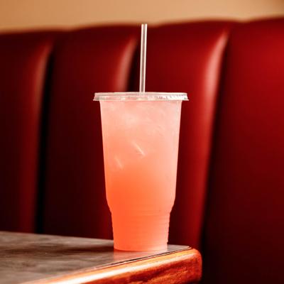 Cold pink drink in a plastic cup on a table, the backdrop is a red booth seating.