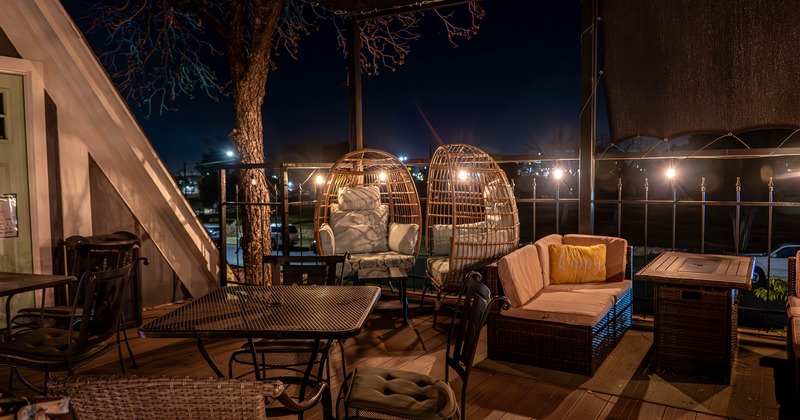 Cozy outdoor terrace at night with wicker seating, cushioned sofas, and hanging egg chairs