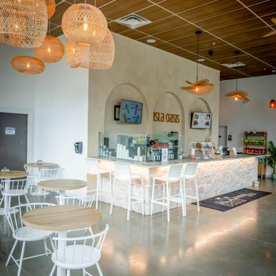 Modern cafe interior with a stone counter, wicker pendant lights, and white chairs.