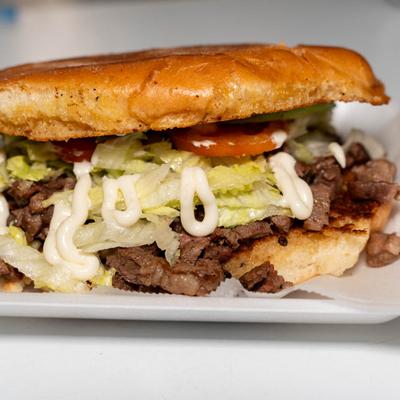 Grilled steak sandwich, with lettuce, cheese sauce, tomato, and avocado.