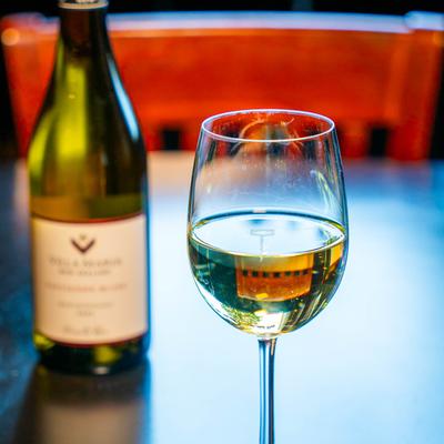 A glass of white wine with a bottle in the background.