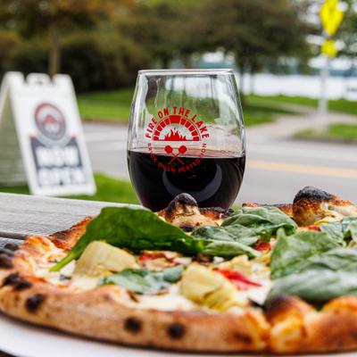 Honeoye Pizza topped with spinach, served on a outdoor table with a drink.