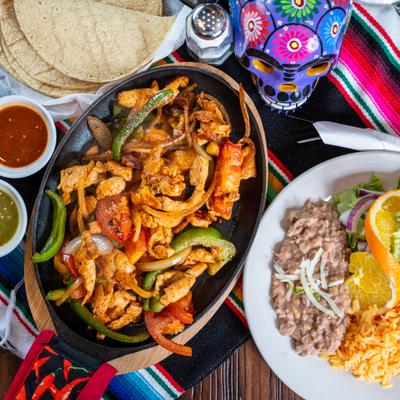 Chicken fajitas served with sides of rice, beans, tortillas, and salsas.