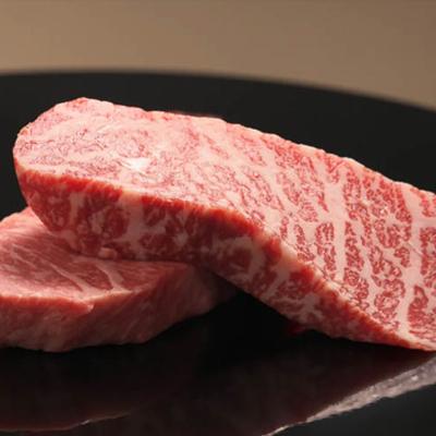 Two pieces of raw beef displayed on a sleek black plate, highlighting its rich color and texture.