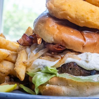 Stacked bacon burger topped with herbed cream cheese, onion rings, and caramelized onions.