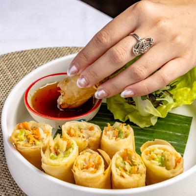 Hand dipping a spring roll into a cup of sweet and sour sauce.